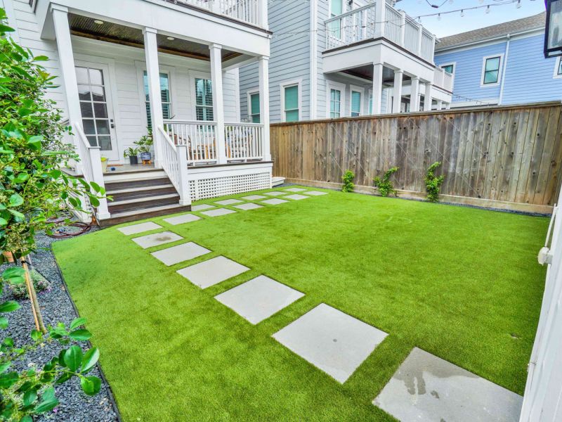 square stepping stones and artificial grass of a white house's backyard - Orion Turf and Landscape